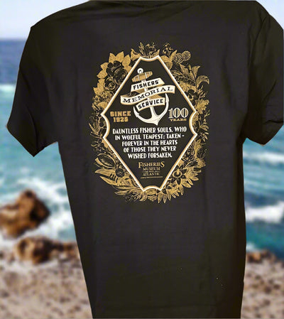Black t-shirt with gold emblem and text against a blurred ocean background